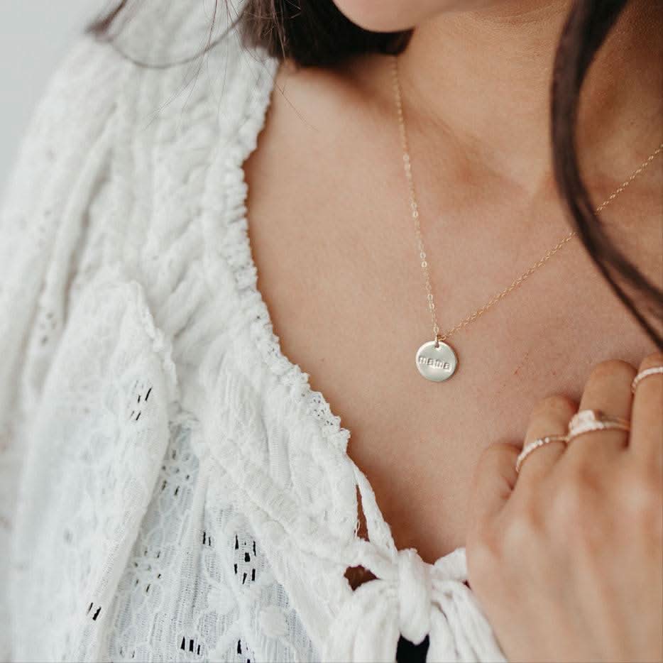 Mama Disc Necklace in gold worn with a white lace top, emphasizing its minimalist design and sentimental value for mothers.