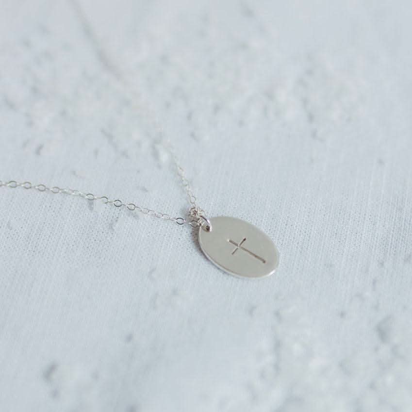 Sterling Silver Oval Cross Necklace by Barberry & Lace Jewelry laid on lace fabric, highlighting its delicate and hypoallergenic craftsmanship.