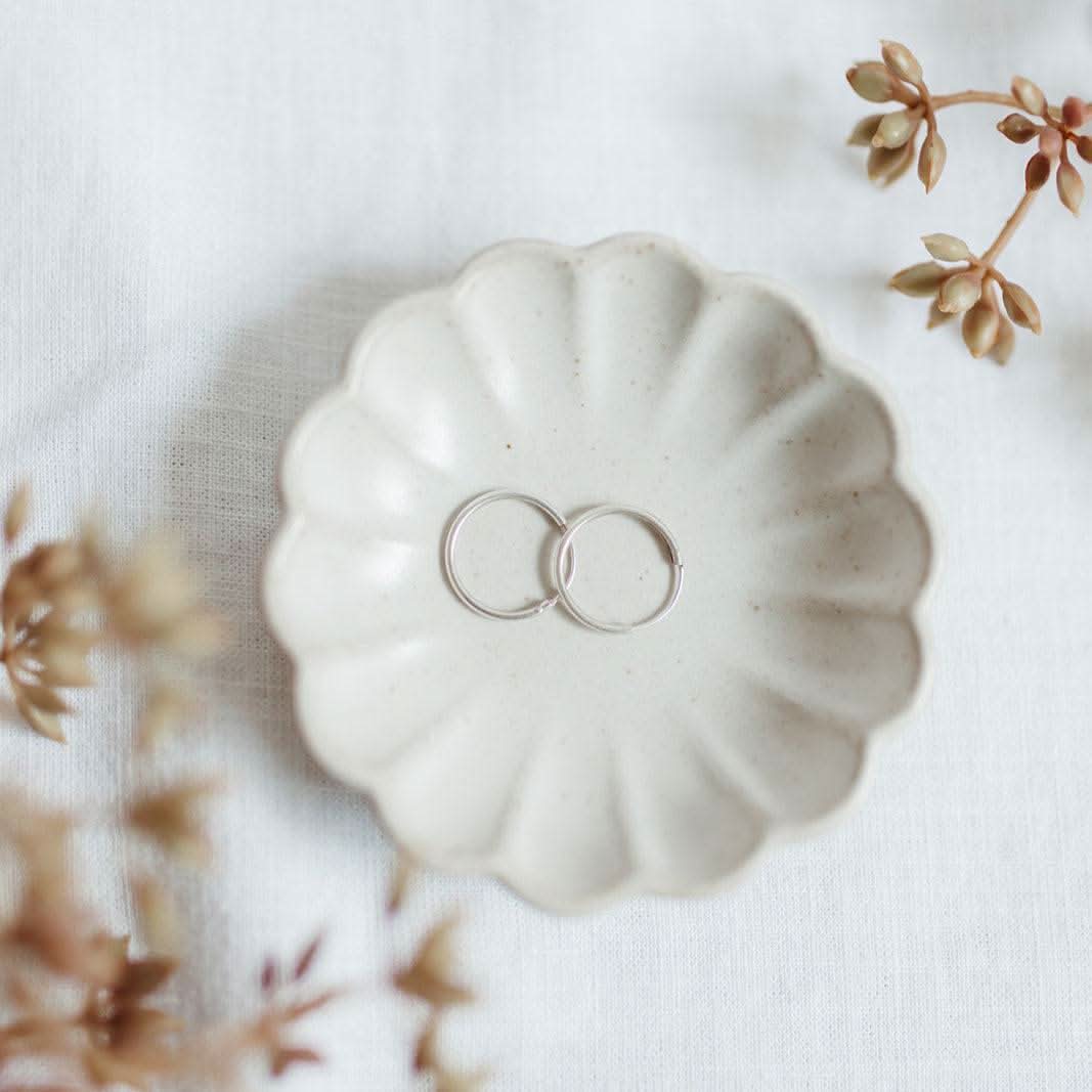 Sterling silver Endless Huggie Hoop Earrings resting in a scalloped ceramic dish, showcasing their sleek, hypoallergenic design.