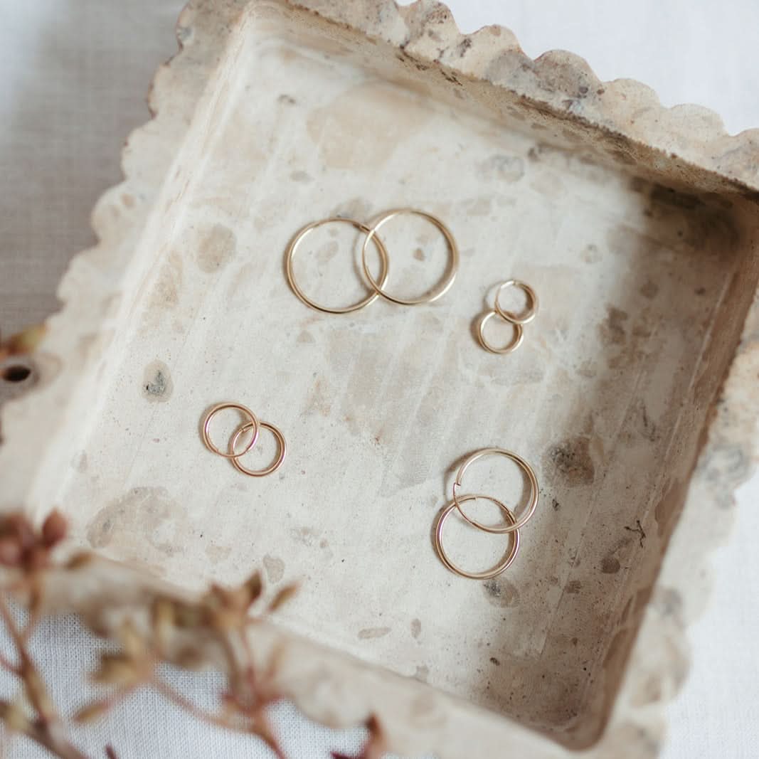 Assorted sizes of Endless Huggie Hoop Earrings in gold fill arranged on a textured stone tray, ideal for layering or solo wear.