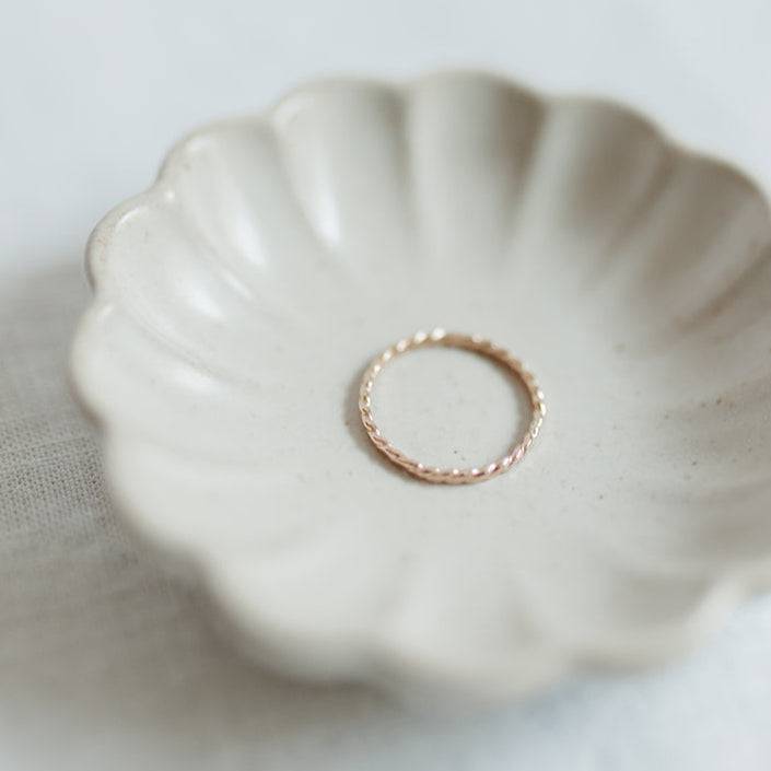 Single Baguette Twisted Stacking Ring in gold displayed in a ceramic dish, emphasizing its minimalist and handcrafted detail.