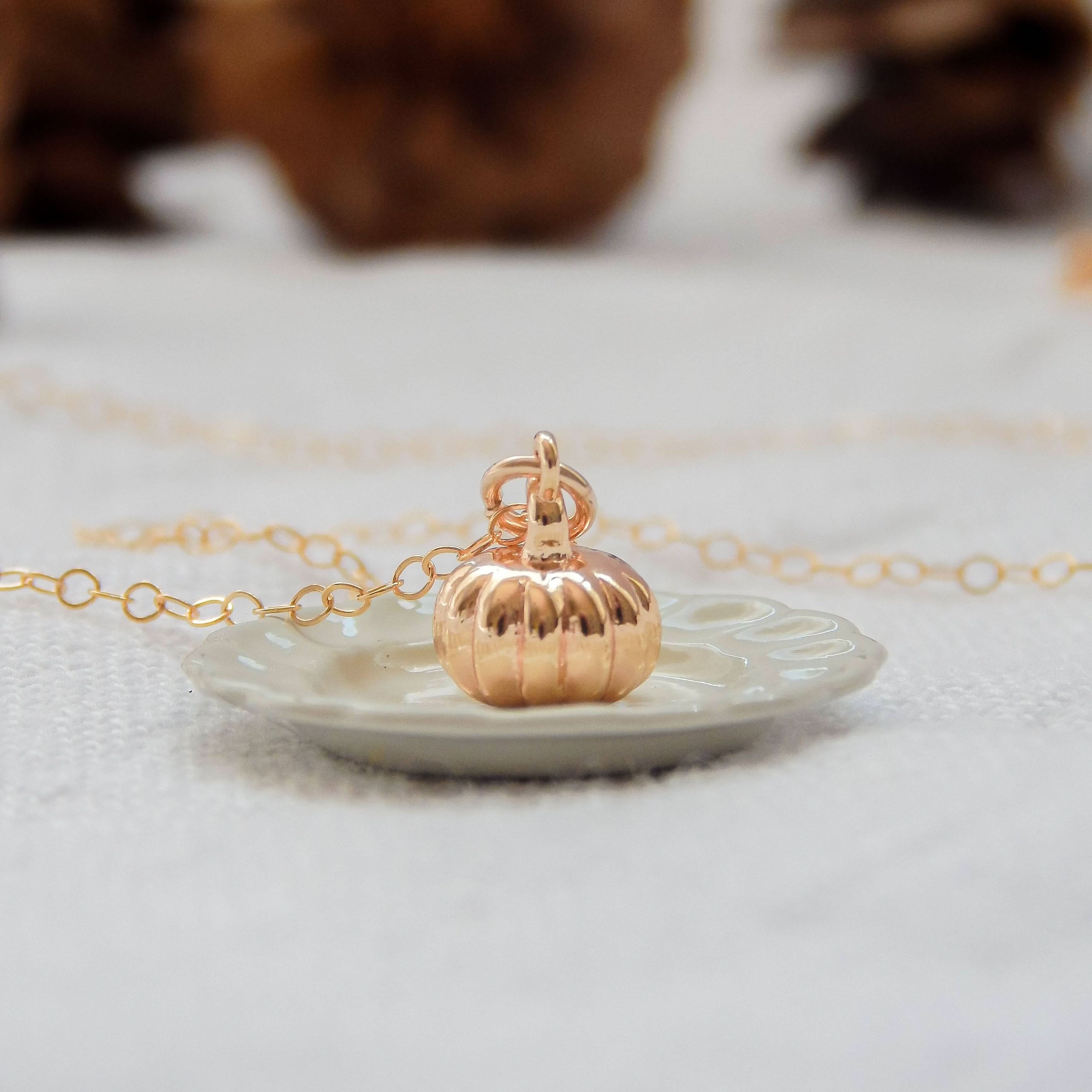 Close-up of gold pumpkin charm necklace on a decorative plate.