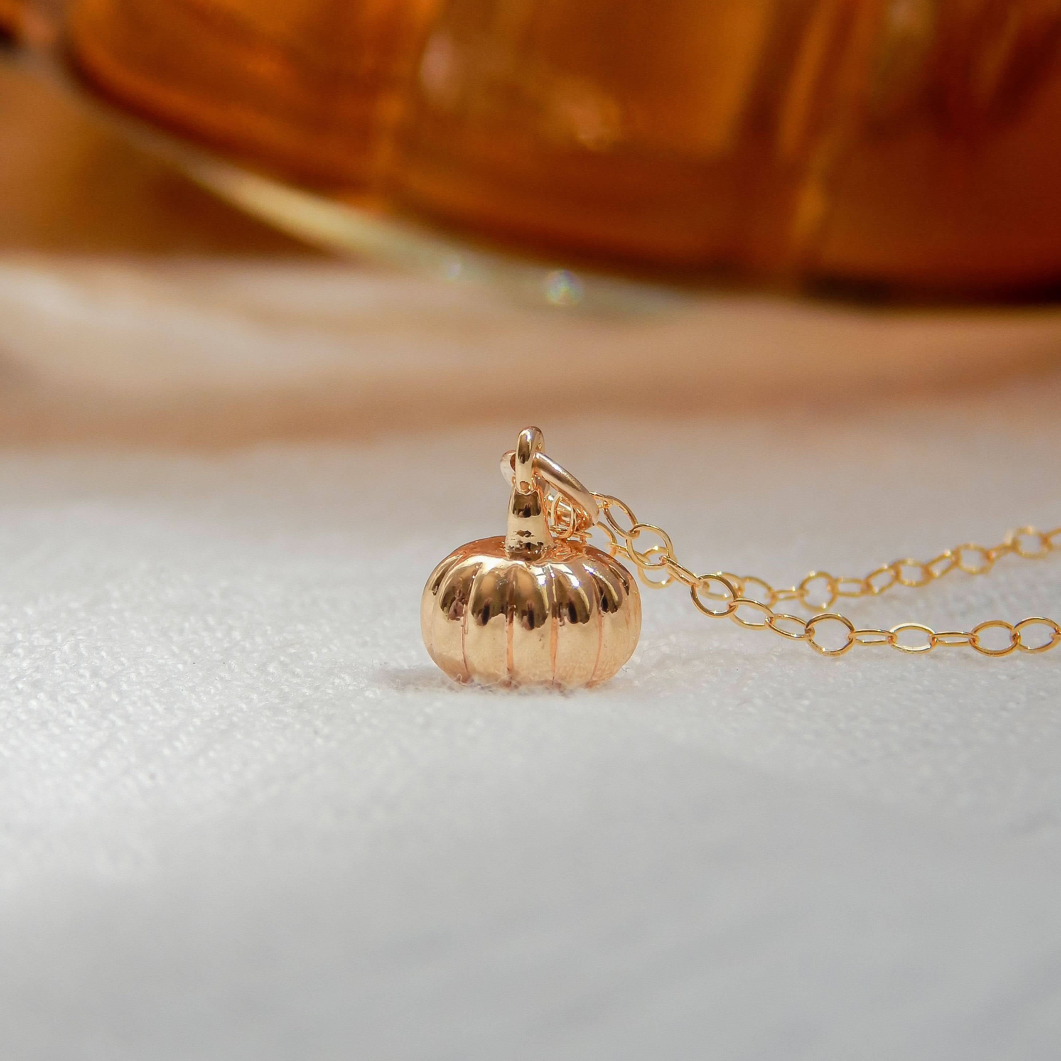 Gold pumpkin charm necklace with a warm, golden background.