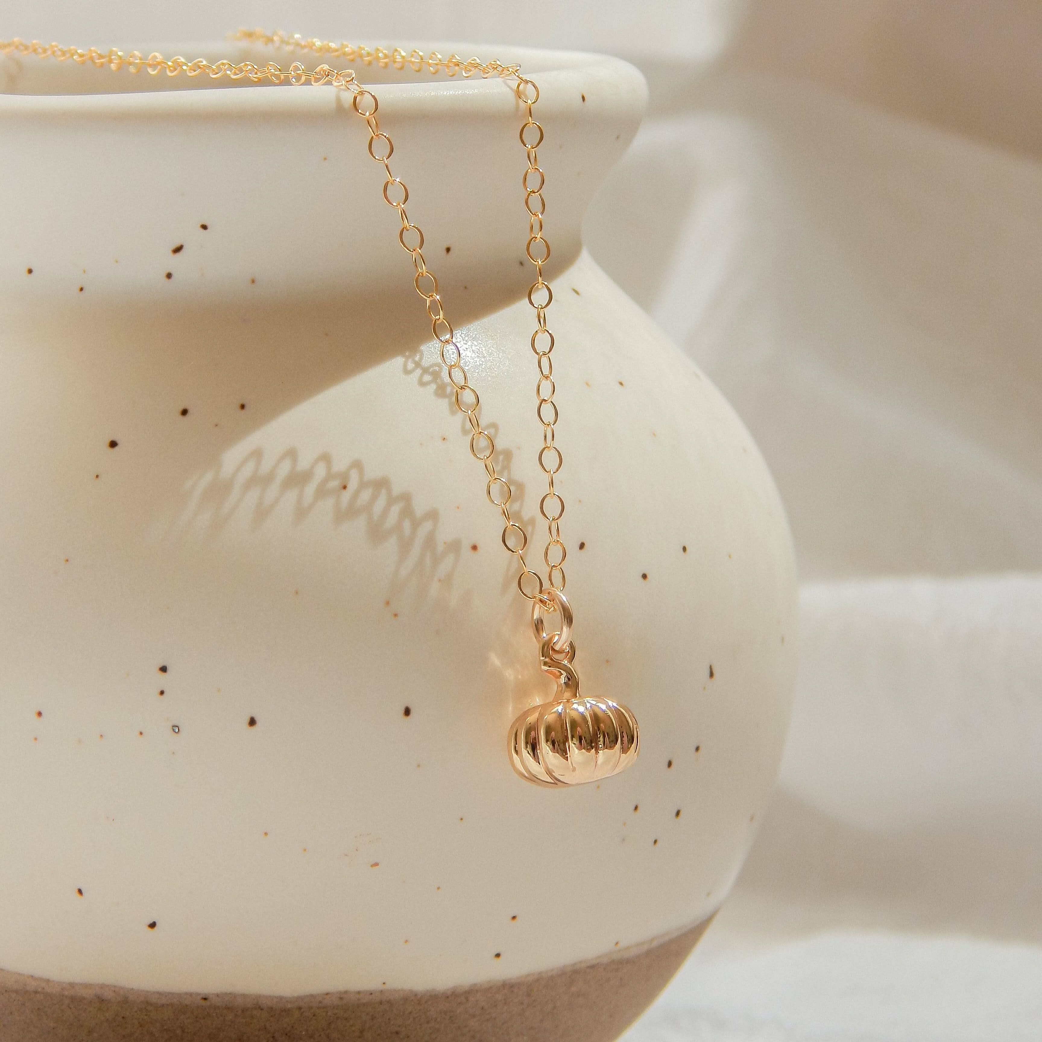 Gold pumpkin charm necklace hanging elegantly on a ceramic vase.
