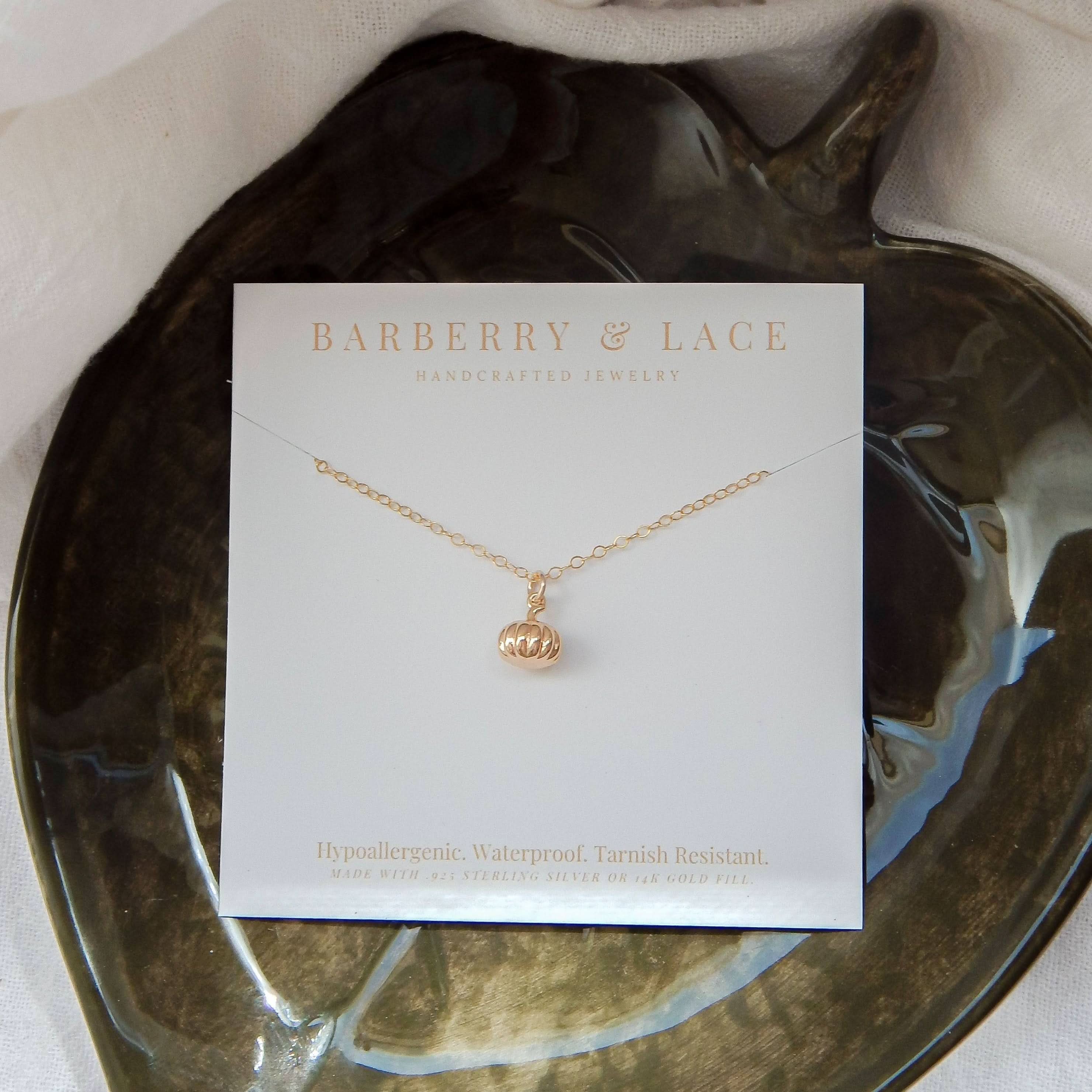 Gold pumpkin charm necklace on a jewelry card placed on a leaf-shaped dish.