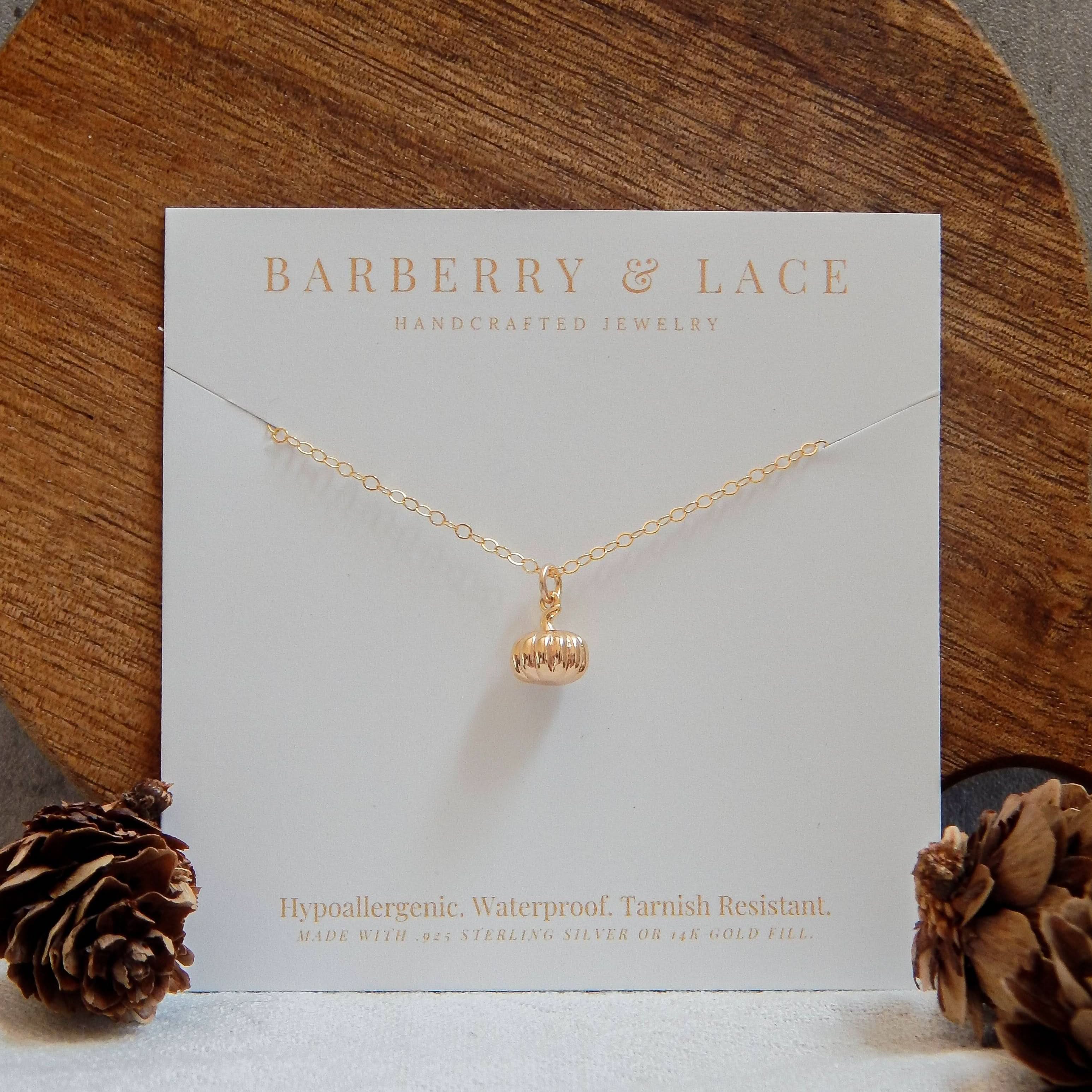 Gold pumpkin charm necklace on branded jewelry card with pinecones.