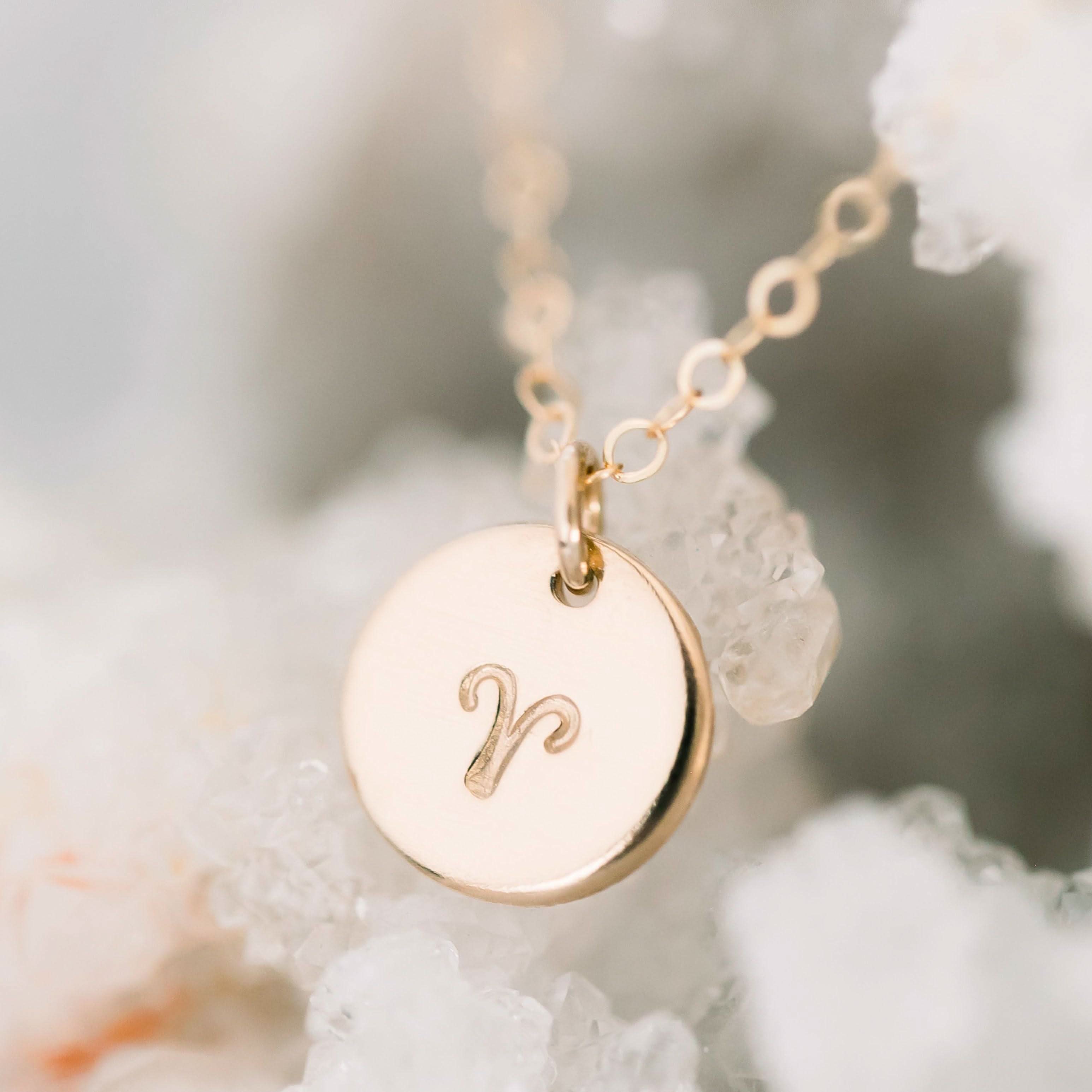 Personalized Zodiac Disc Necklace in 14k gold fill featuring Aries symbol, displayed on a crystal background for celestial elegance.