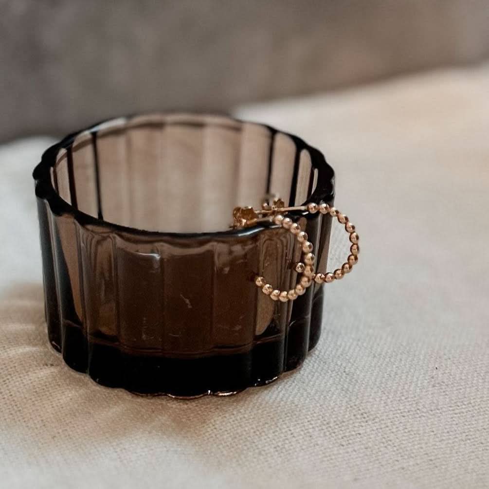 Beaded Huggie Hoop Earrings resting on a dark glass cup. Elegant handcrafted hoops ideal for minimalist jewelry lovers.