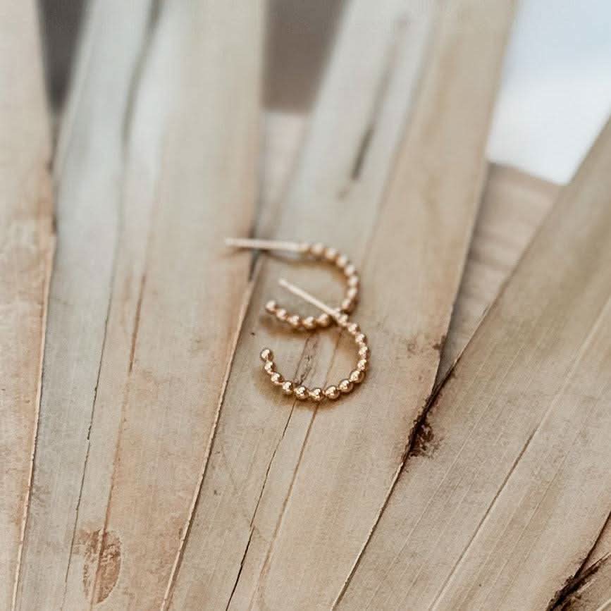 Beaded Huggie Hoop Earrings by Barberry & Lace Jewelry displayed on dried palm leaves. Minimalist 14k gold fill hoops for everyday wear.