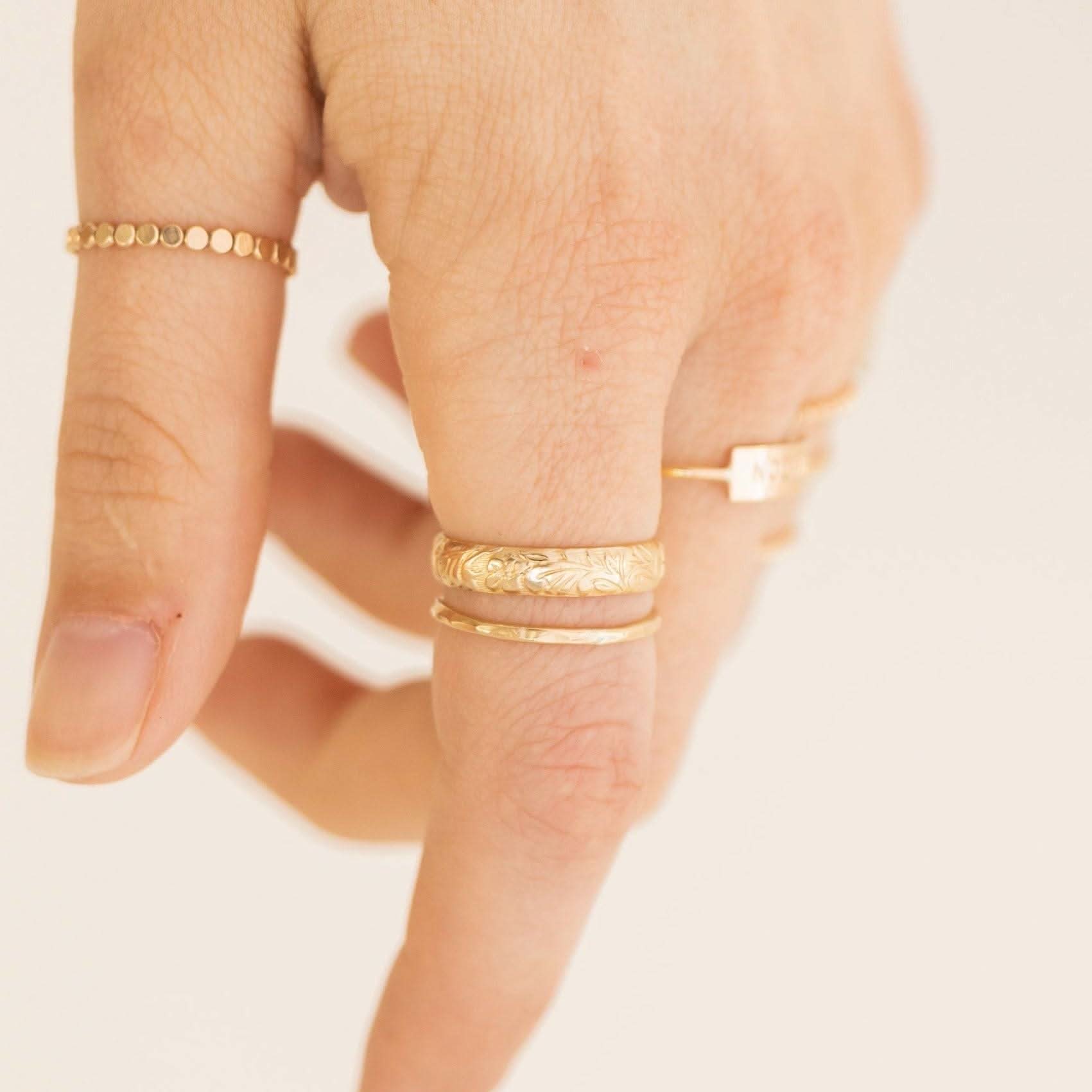 Floral Band Ring styled on hand with other gold rings, showcasing its delicate floral design and stackable versatility.