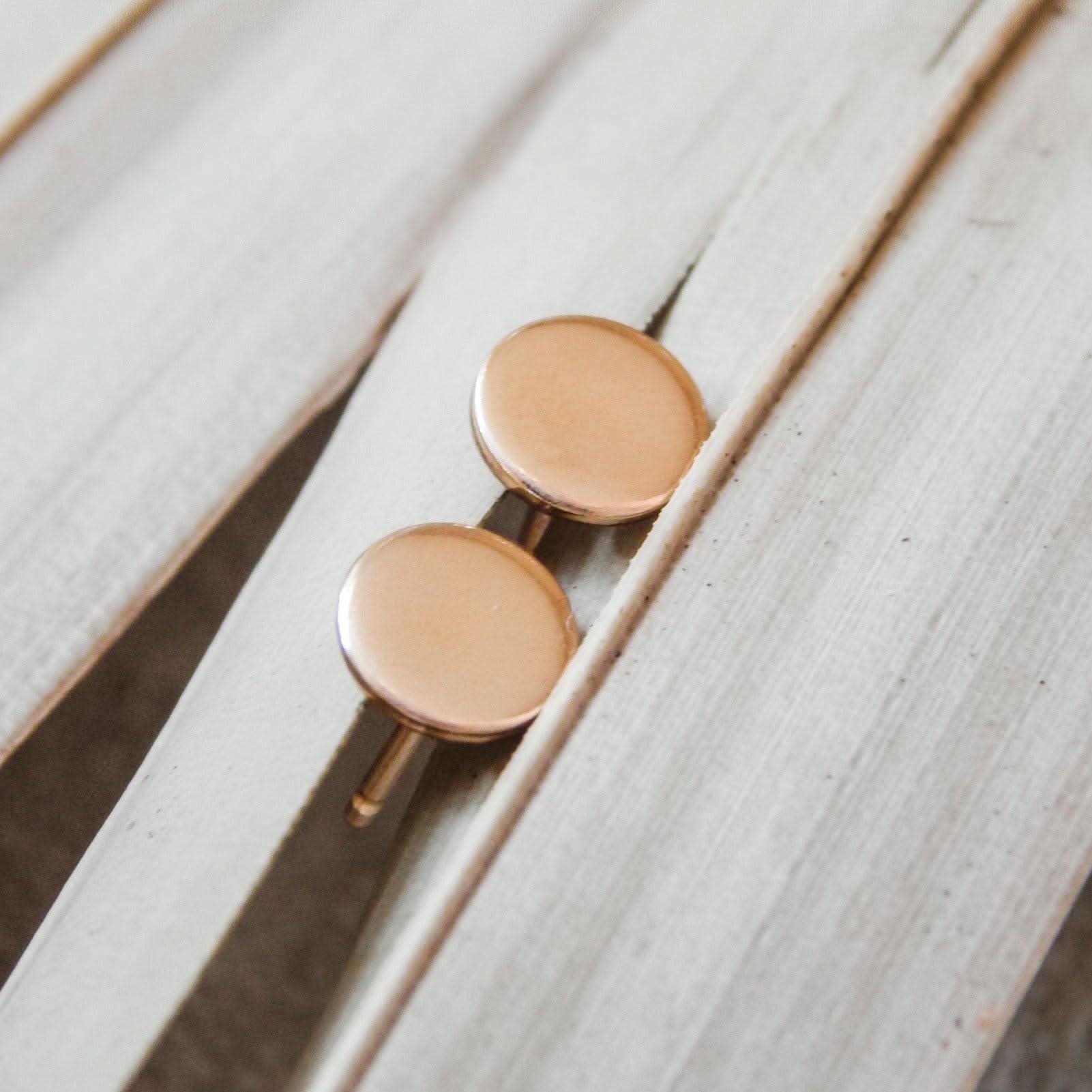 Smooth finish Hypoallergenic Circle Stud Earrings in 14k gold fill resting on neutral-toned leaves. Sleek and modern jewelry style.