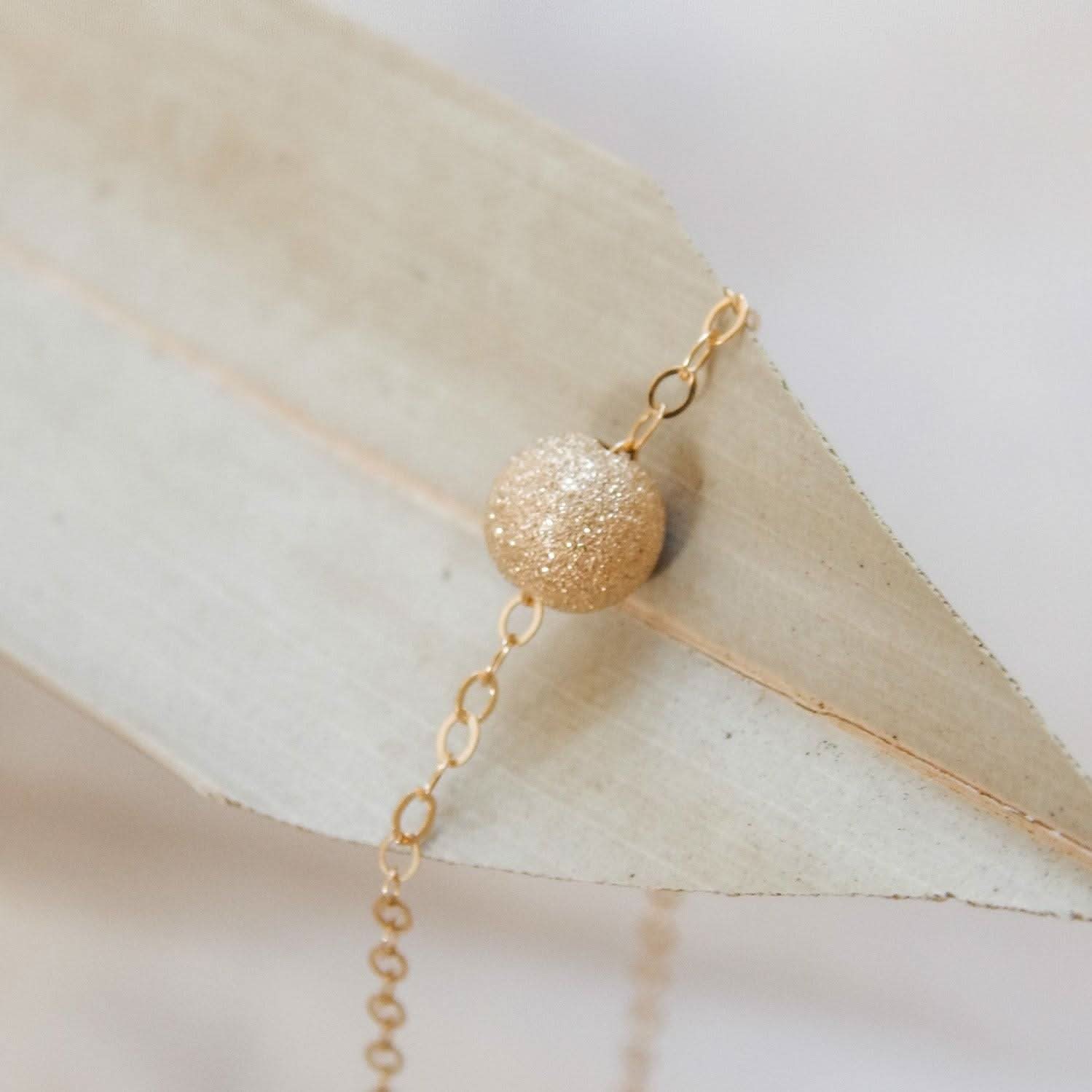 Close-up of the Layering Stardust Bead Necklace by Barberry & Lace Jewelry featuring a single shimmery gold bead on a delicate chain.