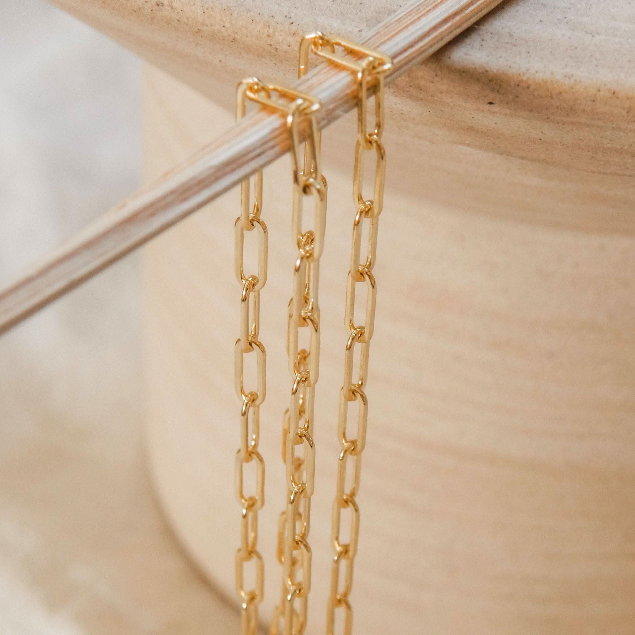 Two Barberry & Lace gold paperclip chain necklaces draped over a ceramic pot, highlighting the delicate and modern link design for layering.