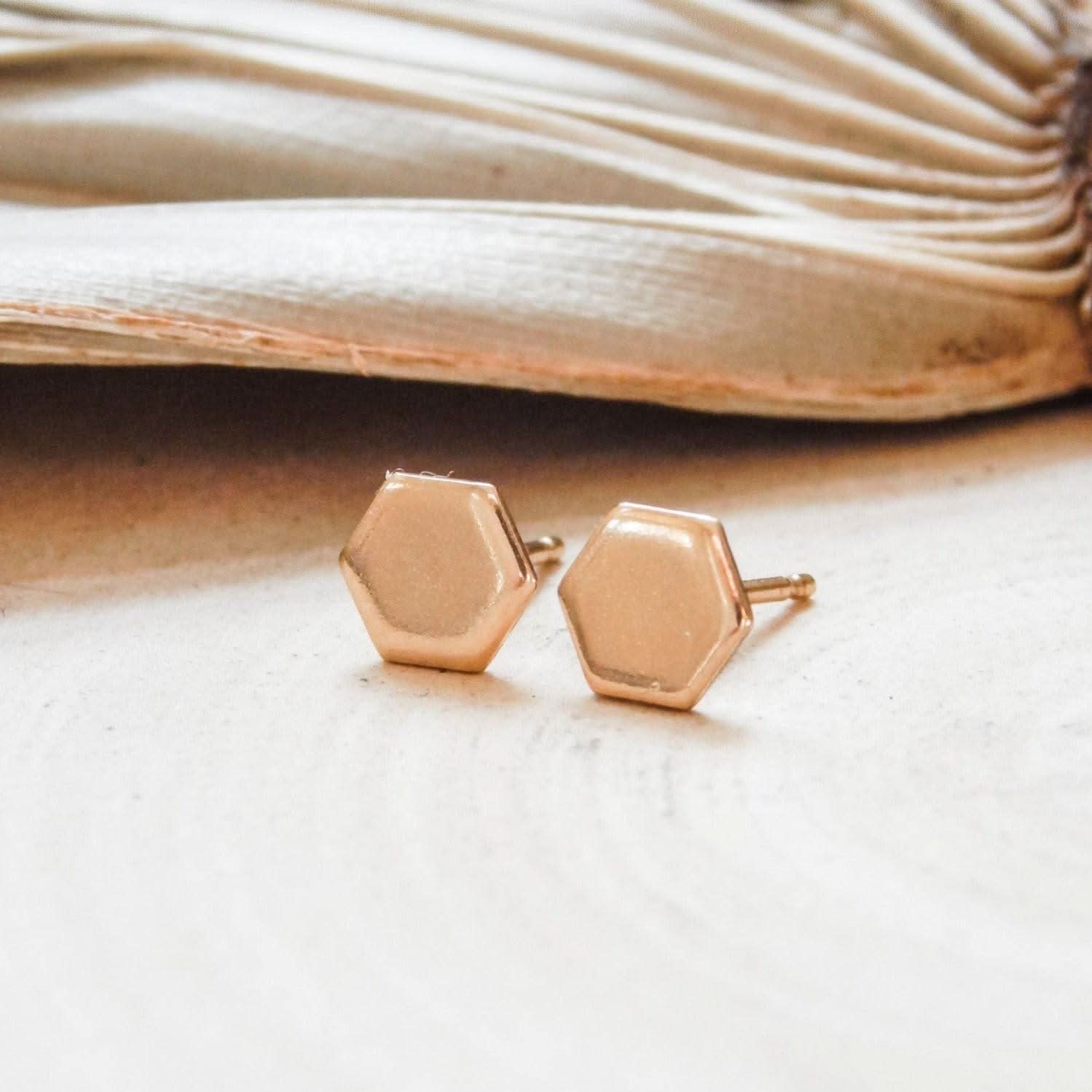 Hypoallergenic hexagon stud earrings in 14k gold fill, displayed on a neutral surface. Minimalist geometric design for everyday wear.