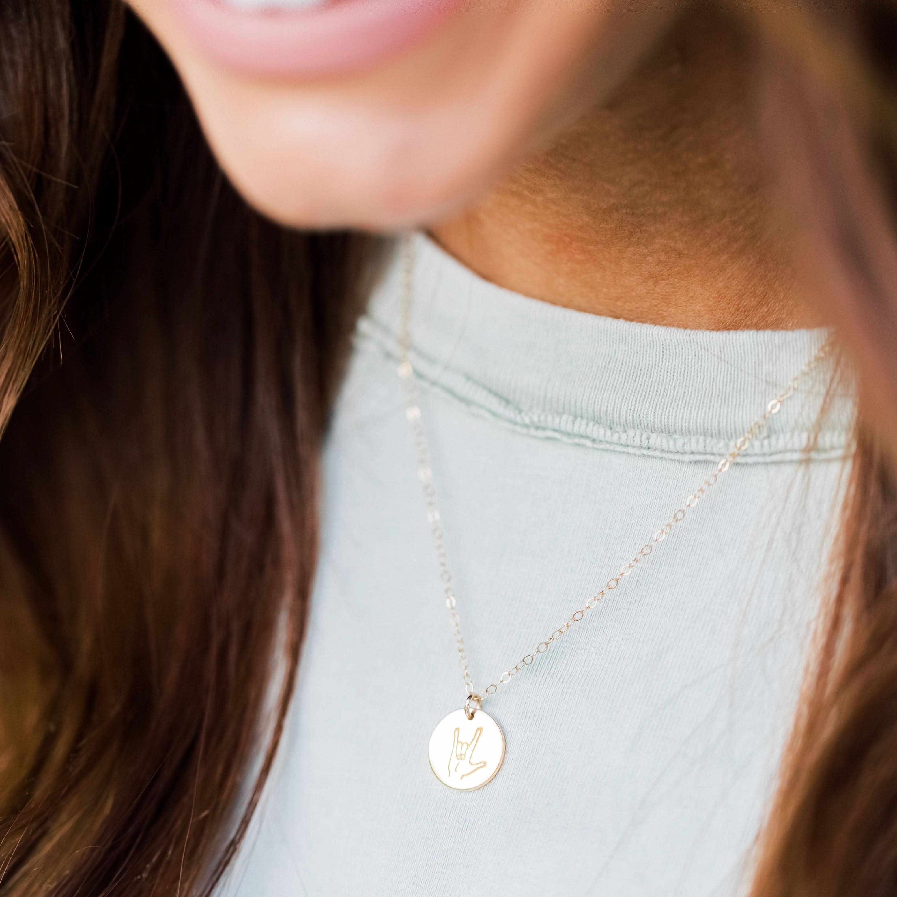 Woman wearing ASL 'I Love You' Sign Language Disc Necklace by Barberry & Lace, showcasing minimalist gold jewelry style.