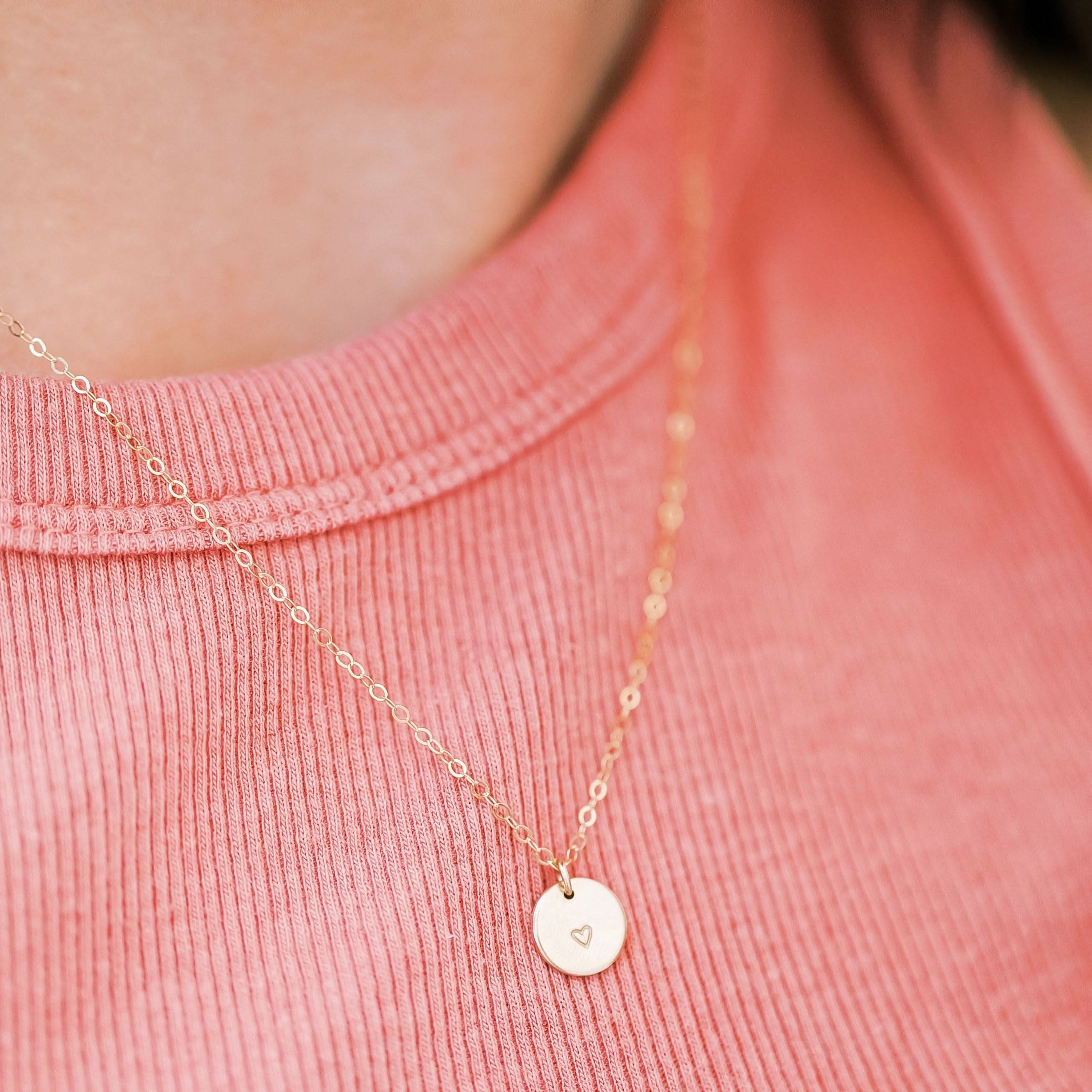 Barberry & Lace heart disc necklace worn with pink top, showcasing dainty gold chain and stamped heart pendant. Ideal for daily elegance.