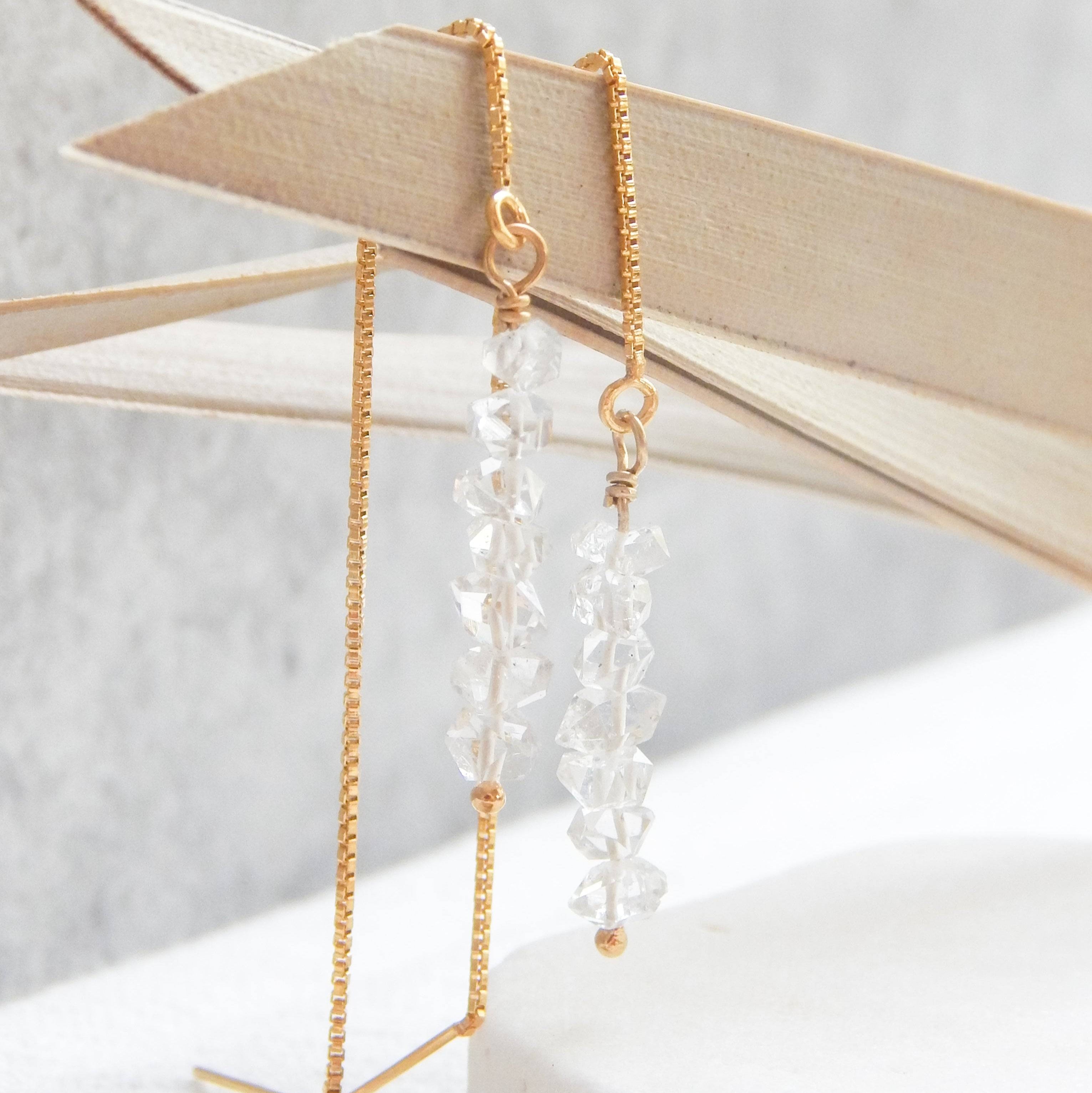 Close-up of Herkimer Diamond Threaded Earrings hanging on wooden decor. Elegant raw crystals on a delicate gold thread chain.