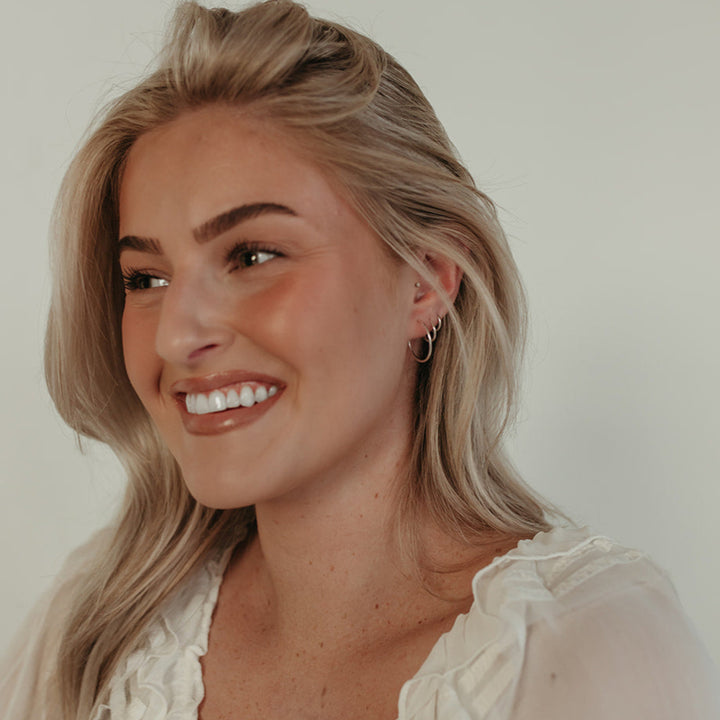 Smiling model wearing Endless Huggie Hoop Earrings in gold fill, highlighting their lightweight and versatile everyday appeal.