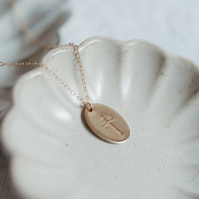 Oval Cross Necklace in 14k Gold Fill by Barberry & Lace Jewelry displayed in a scalloped ceramic dish, ideal for faith-inspired everyday wear.