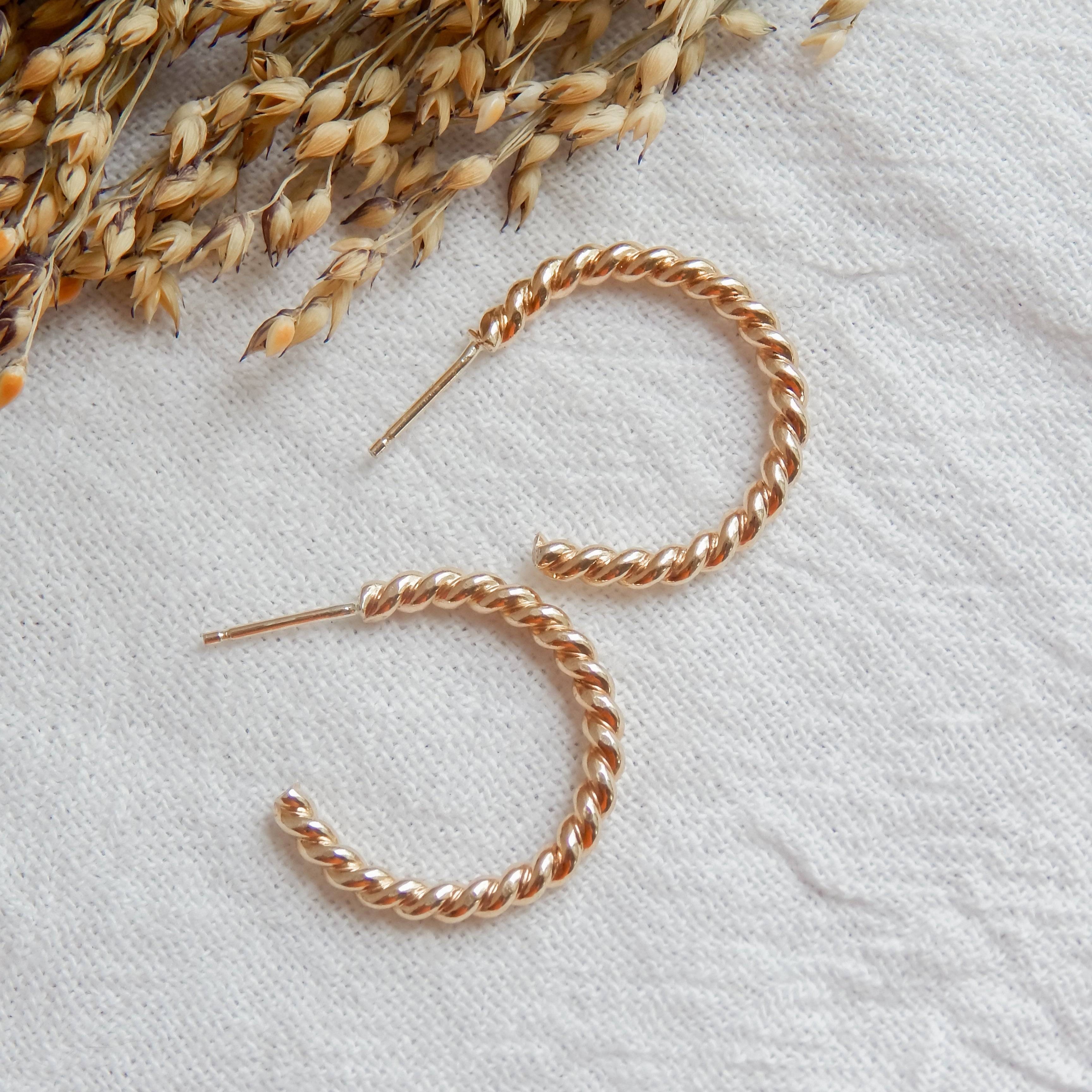 Twist Hoop Earrings by Barberry & Lace Jewelry in gold-tone finish, displayed on textured fabric with dried wheat accents. Hypoallergenic and waterproof.