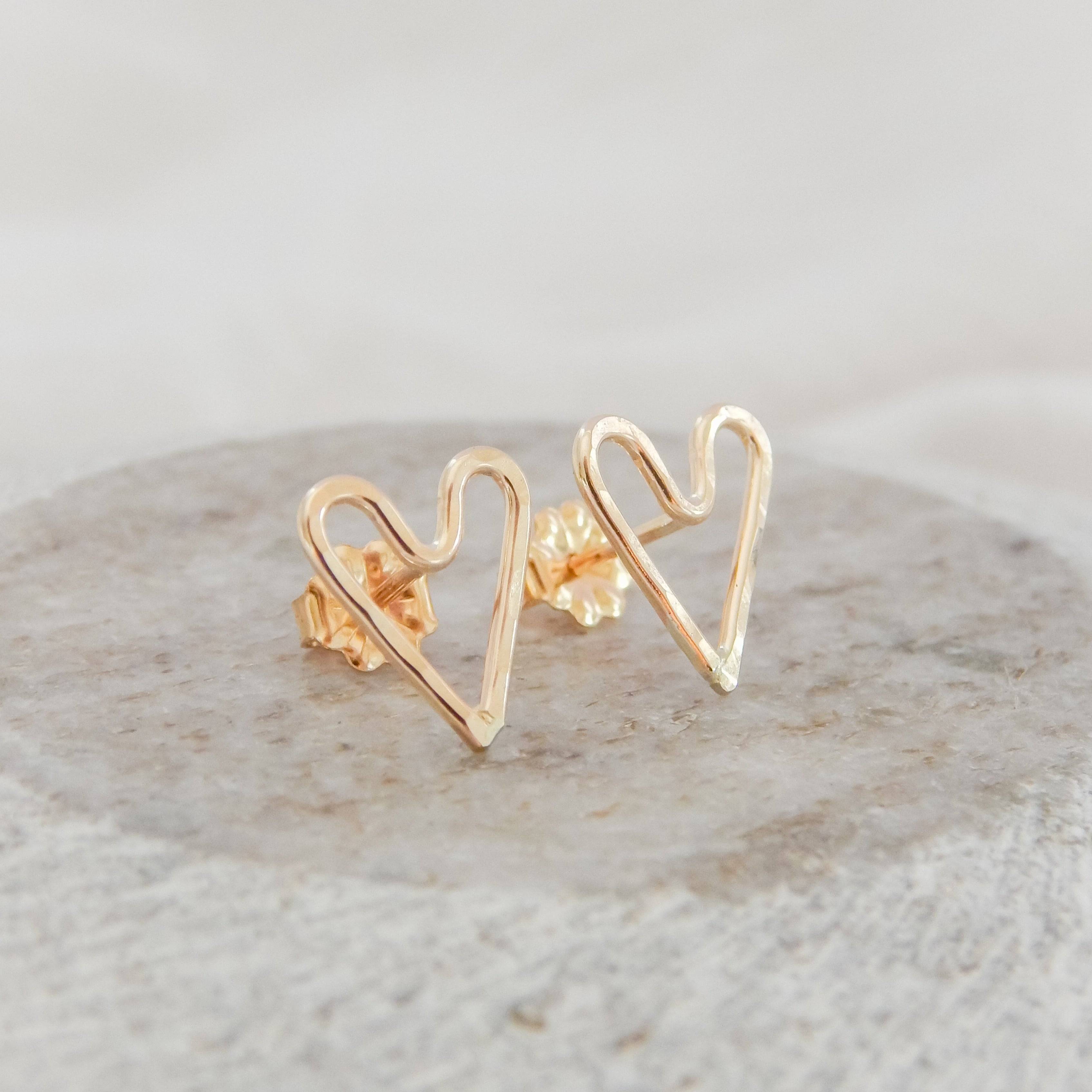 Hammered Heart Stud Earrings by Barberry & Lace Jewelry shown on a stone surface, handcrafted in 14k gold filled metal with a delicate heart shape.