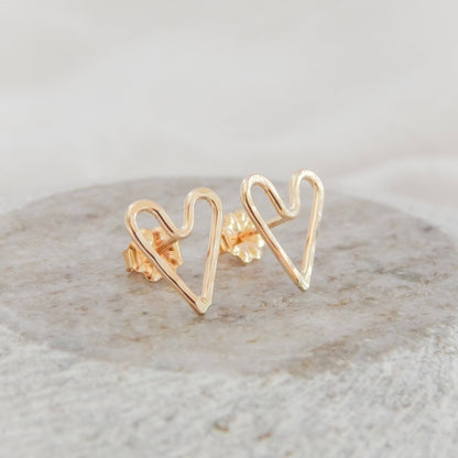 Hammered Heart Stud Earrings by Barberry & Lace Jewelry shown on a stone surface, handcrafted in 14k gold filled metal with a delicate heart shape.