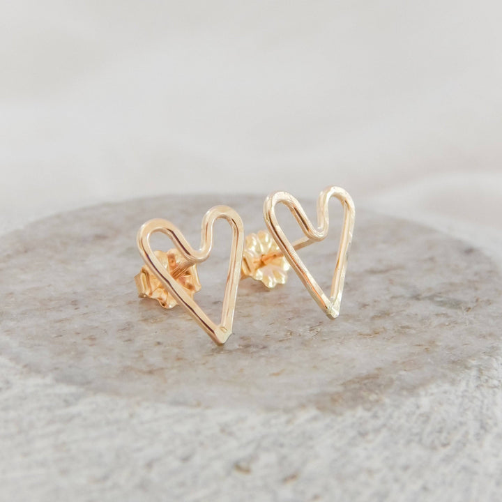 Hammered Heart Stud Earrings by Barberry & Lace Jewelry shown on a stone surface, handcrafted in 14k gold filled metal with a delicate heart shape.