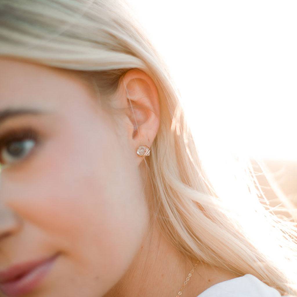 Model wearing Herkimer Diamond Stud Earrings from Barberry & Lace Jewelry, showcasing the minimalist gold-wrapped crystal design in natural sunlight.