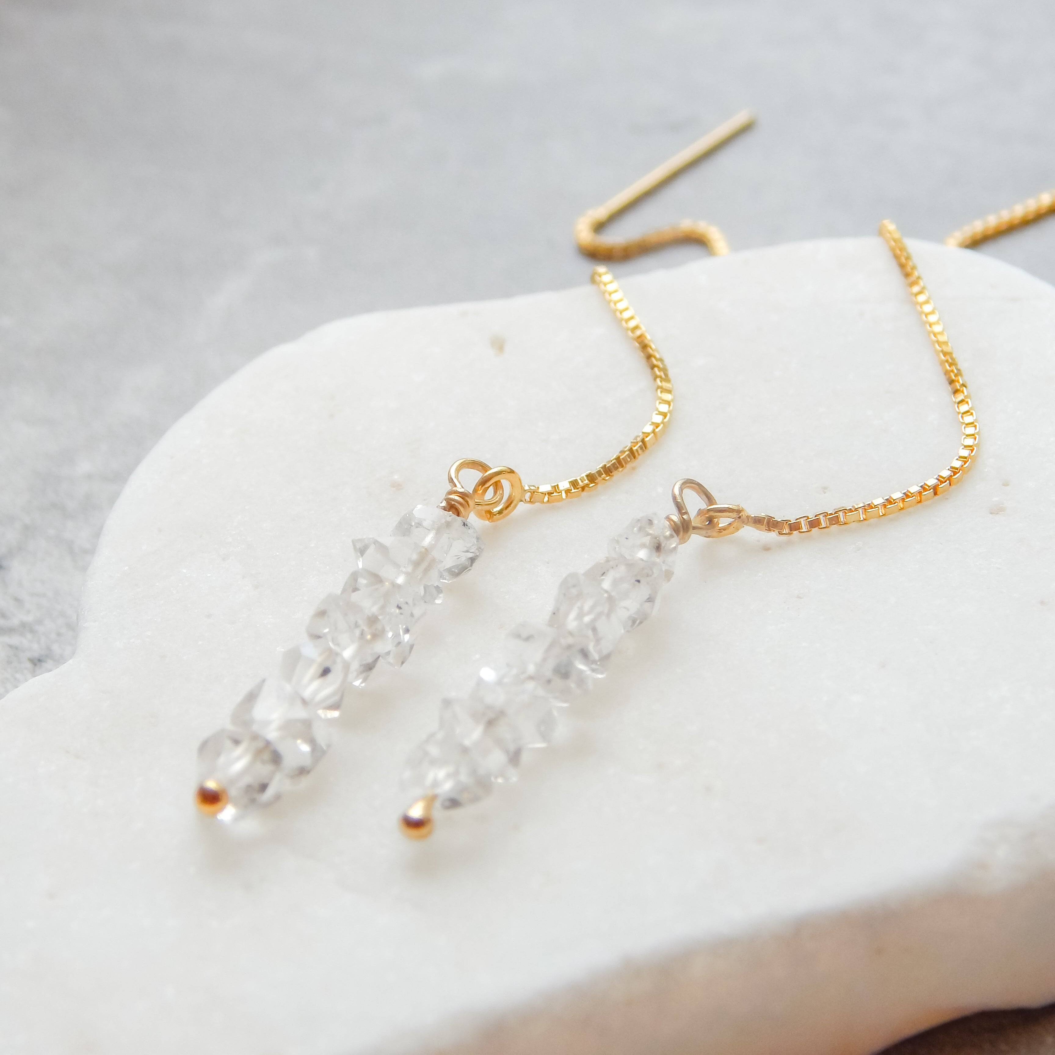 Detailed view of Herkimer Diamond Threaded Earrings on white stone. Features raw crystal clusters and 14k gold fill thread chain.