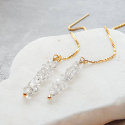 Detailed view of Herkimer Diamond Threaded Earrings on white stone. Features raw crystal clusters and 14k gold fill thread chain.
