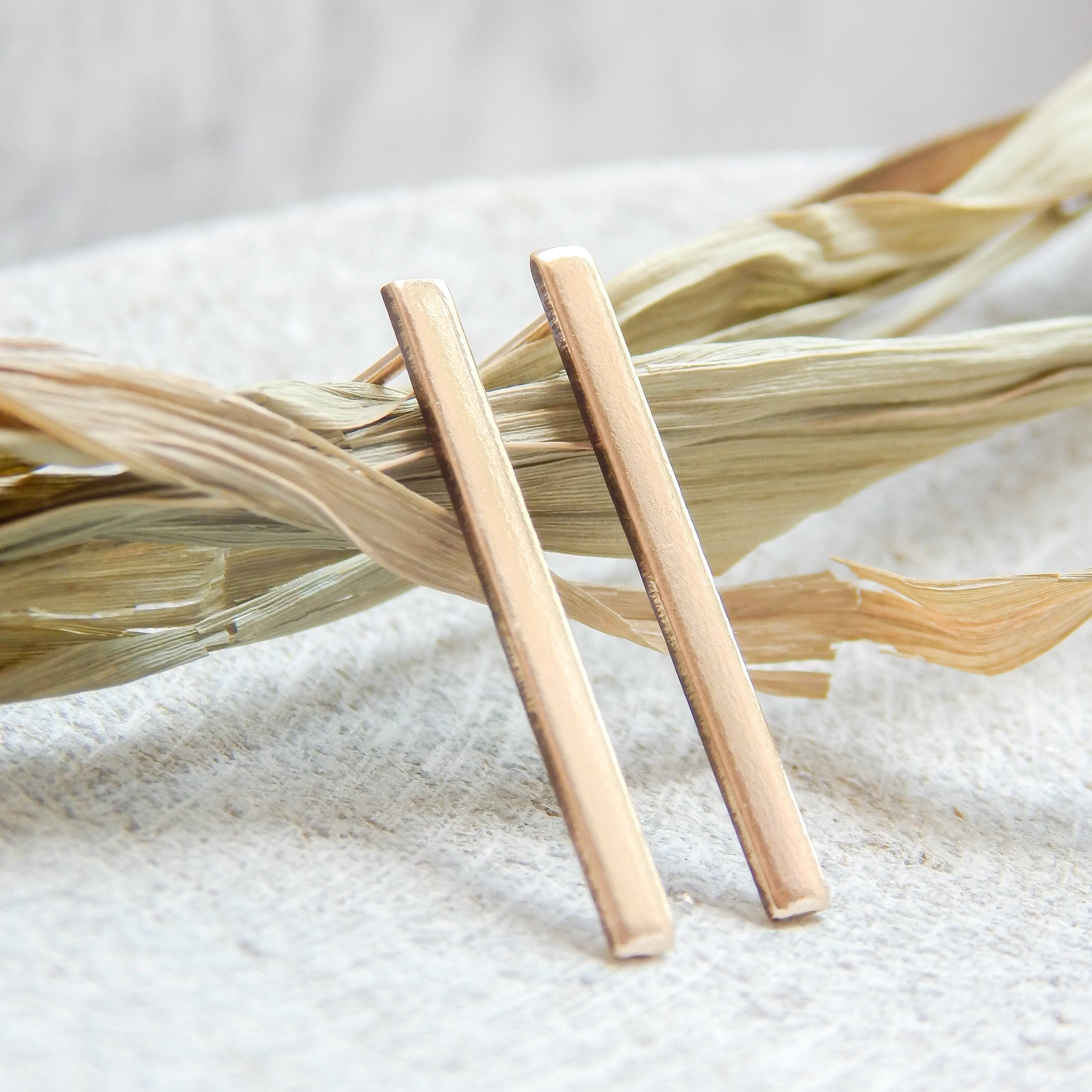 Stick Stud Earrings by Barberry & Lace Jewelry in 14k Gold Fill, displayed on textured fabric with dried leaves. Minimalist and waterproof design.