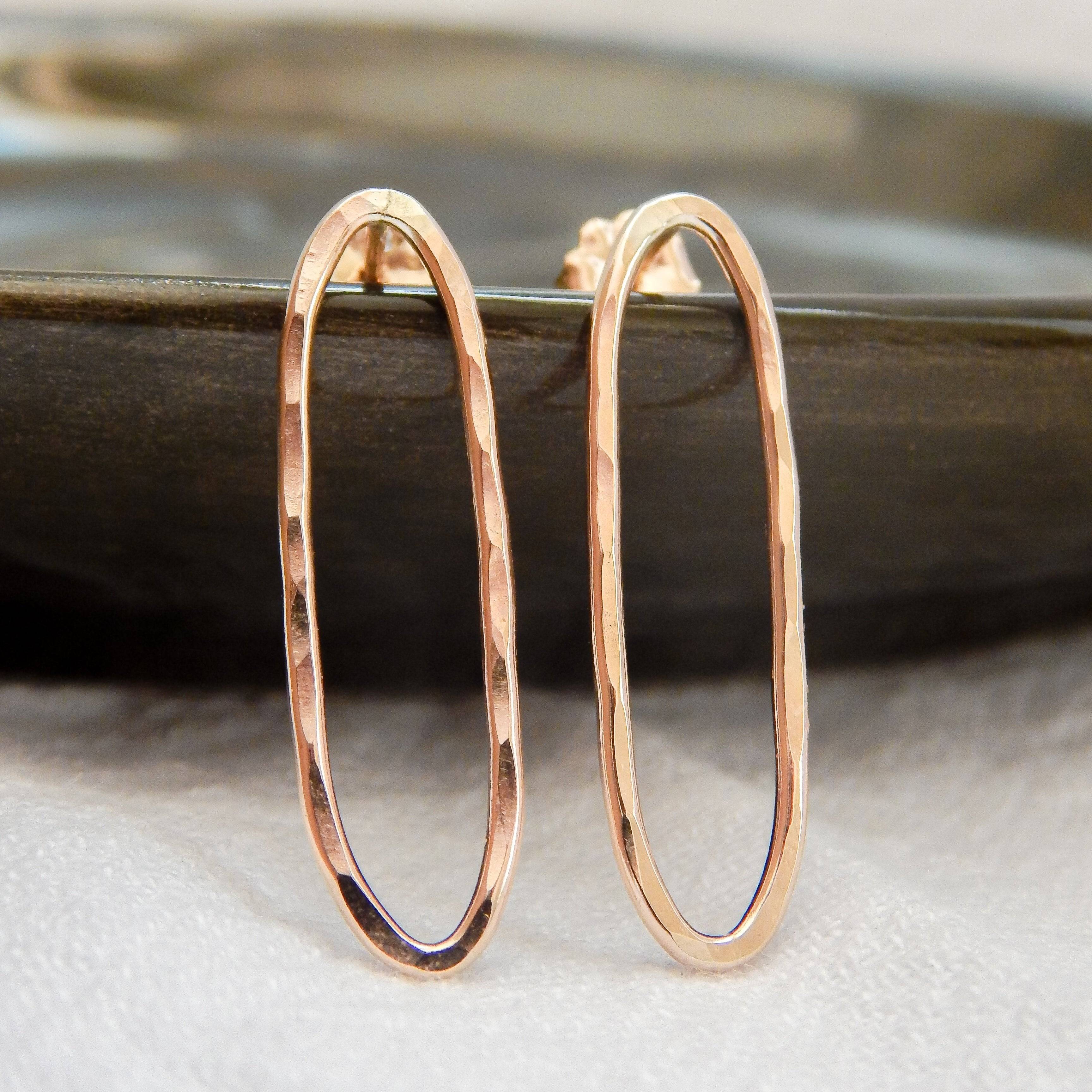 Hammered oval stud earrings in gold finish displayed on a dark dish.