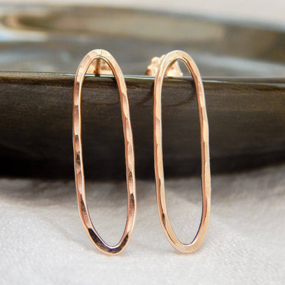 Hammered oval stud earrings in gold finish displayed on a dark dish.