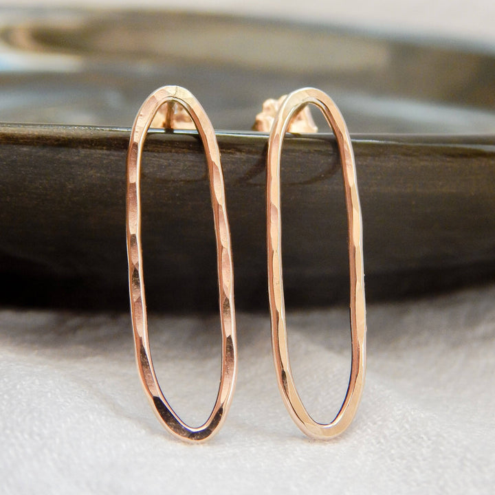 Hammered oval stud earrings in gold finish displayed on a dark dish.