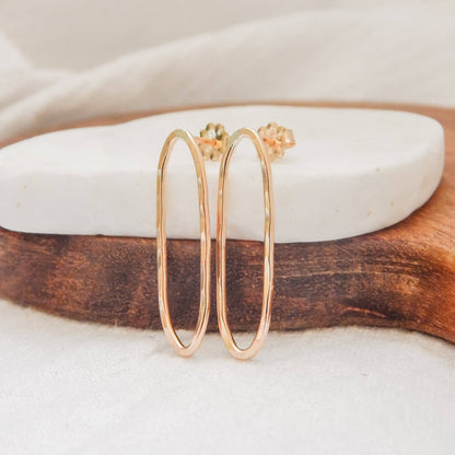 Hammered oval stud earrings in gold on a white stone and wooden display.