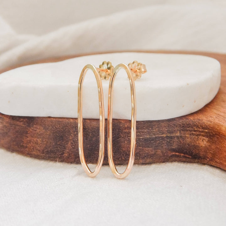 Hammered oval stud earrings in gold on a white stone and wooden display.