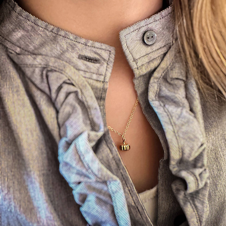 Gold pumpkin charm necklace worn with a ruffled gray blouse.