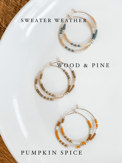 Three Fall Edition - Beaded Hoop Earrings styles labeled Sweater Weather, Wood & Pine, and Pumpkin Spice on a white plate. Seasonal jewelry collection.