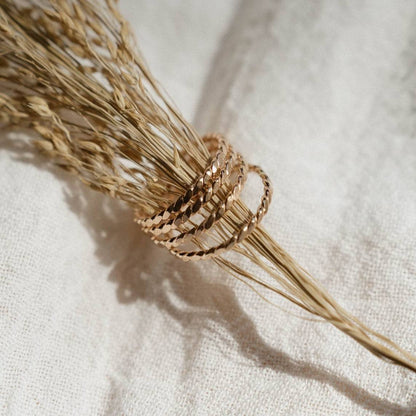 Set of Baguette Twisted Stacking Rings in 14k Gold Fill displayed on dried wheat, showcasing their elegant twisted design and stackable style.