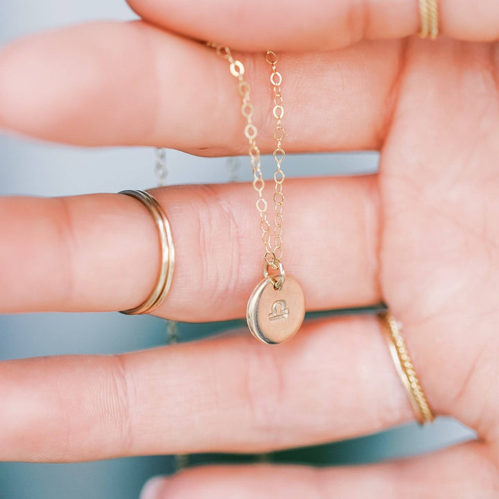 Hand holding a Personalized Zodiac Disc Necklace with Libra charm in gold fill, showcasing delicate chain and minimalist design.