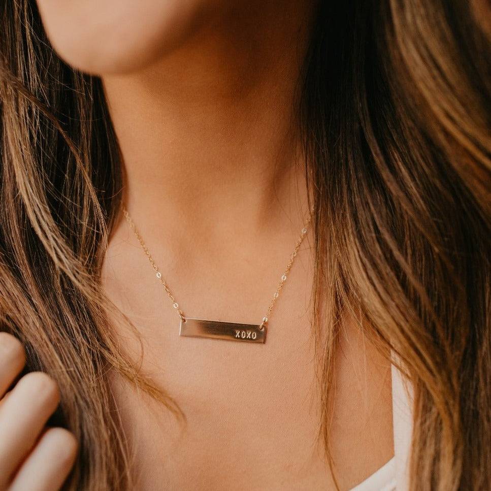Hand Stamped XOXO Bar Necklace by Barberry & Lace in 14k Gold Fill, worn on model. A minimalist, hypoallergenic jewelry piece for everyday wear.
