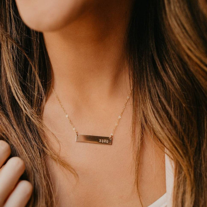 Hand Stamped XOXO Bar Necklace by Barberry & Lace in 14k Gold Fill, worn on model. A minimalist, hypoallergenic jewelry piece for everyday wear.