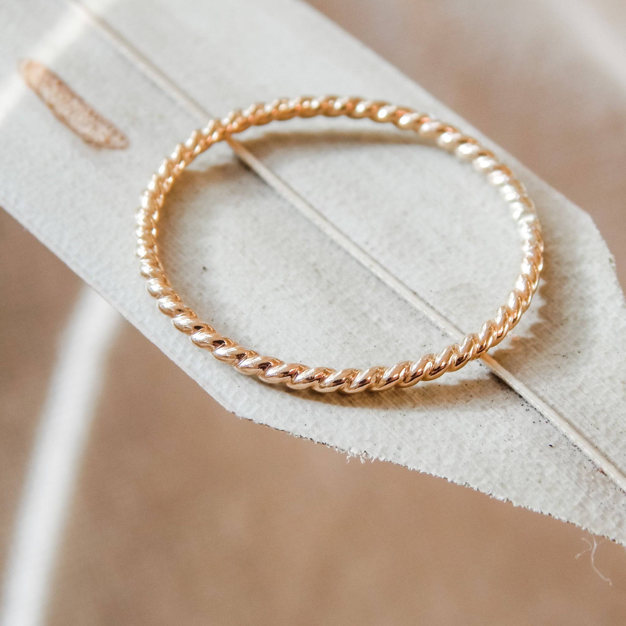 Close-up of a single Petite Twisted Stacking Ring in gold fill resting on a soft beige leaf. Elegant and hypoallergenic design.