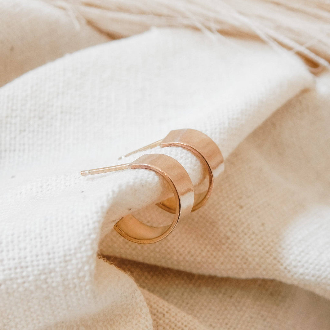 Close-up of Thick Huggie Hoop Stud Earrings in gold fill resting on neutral fabric, highlighting their smooth, chunky hoop style.