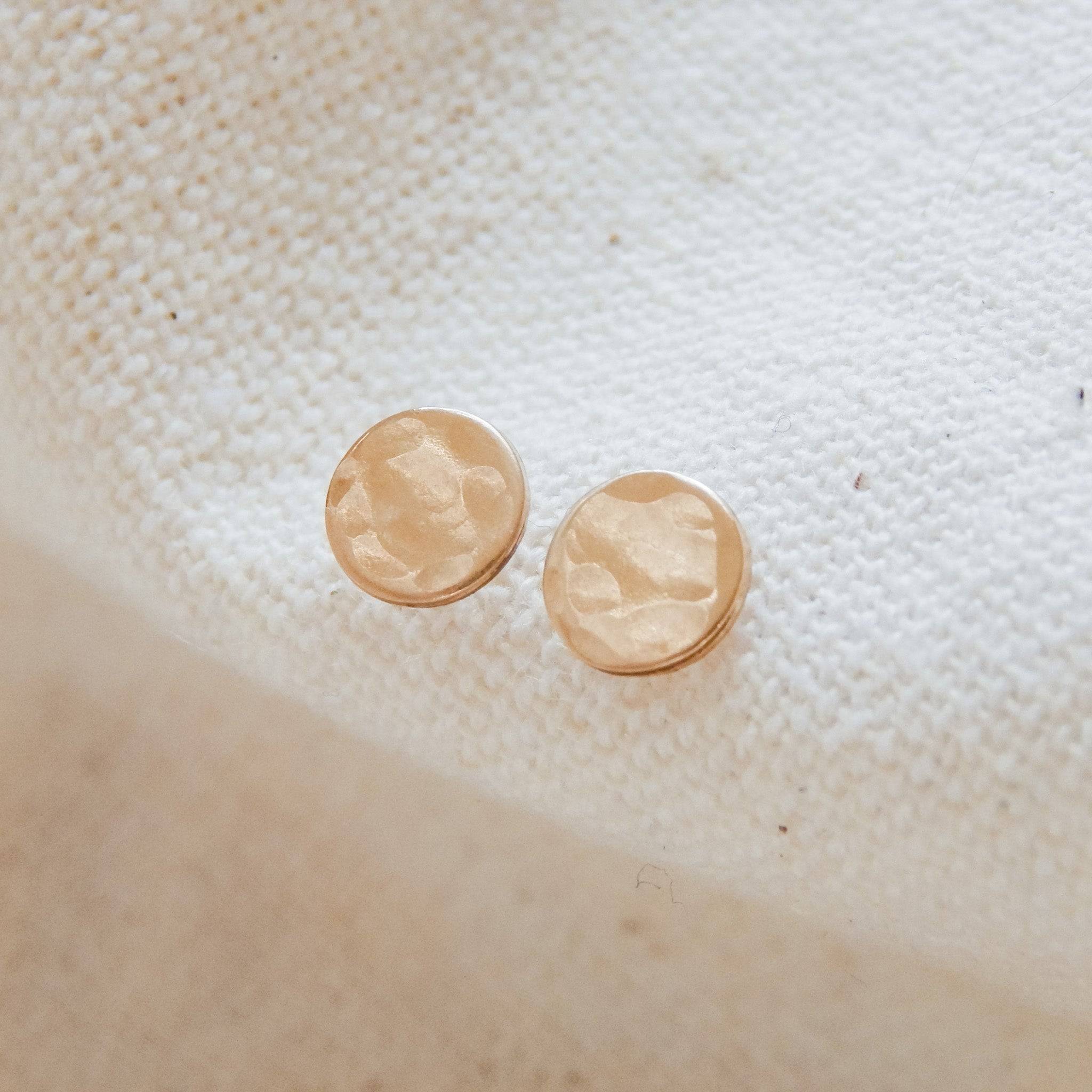 Hypoallergenic Circle Stud Earrings in hammered 14k gold fill on fabric background. Minimalist design ideal for everyday wear.