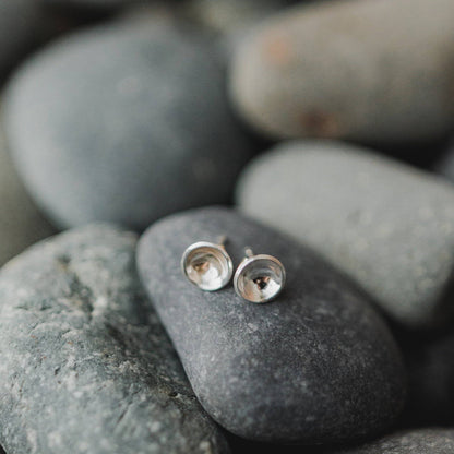 Sterling Silver Concave Disc Stud Earrings resting on smooth stones, reflecting their elegant and hypoallergenic craftsmanship.