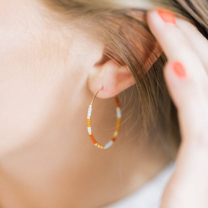 Model wearing Summer Edition - Beaded Hoop Earrings in Desert Sunrise colorway, showcasing lightweight boho style with gold and orange beads.