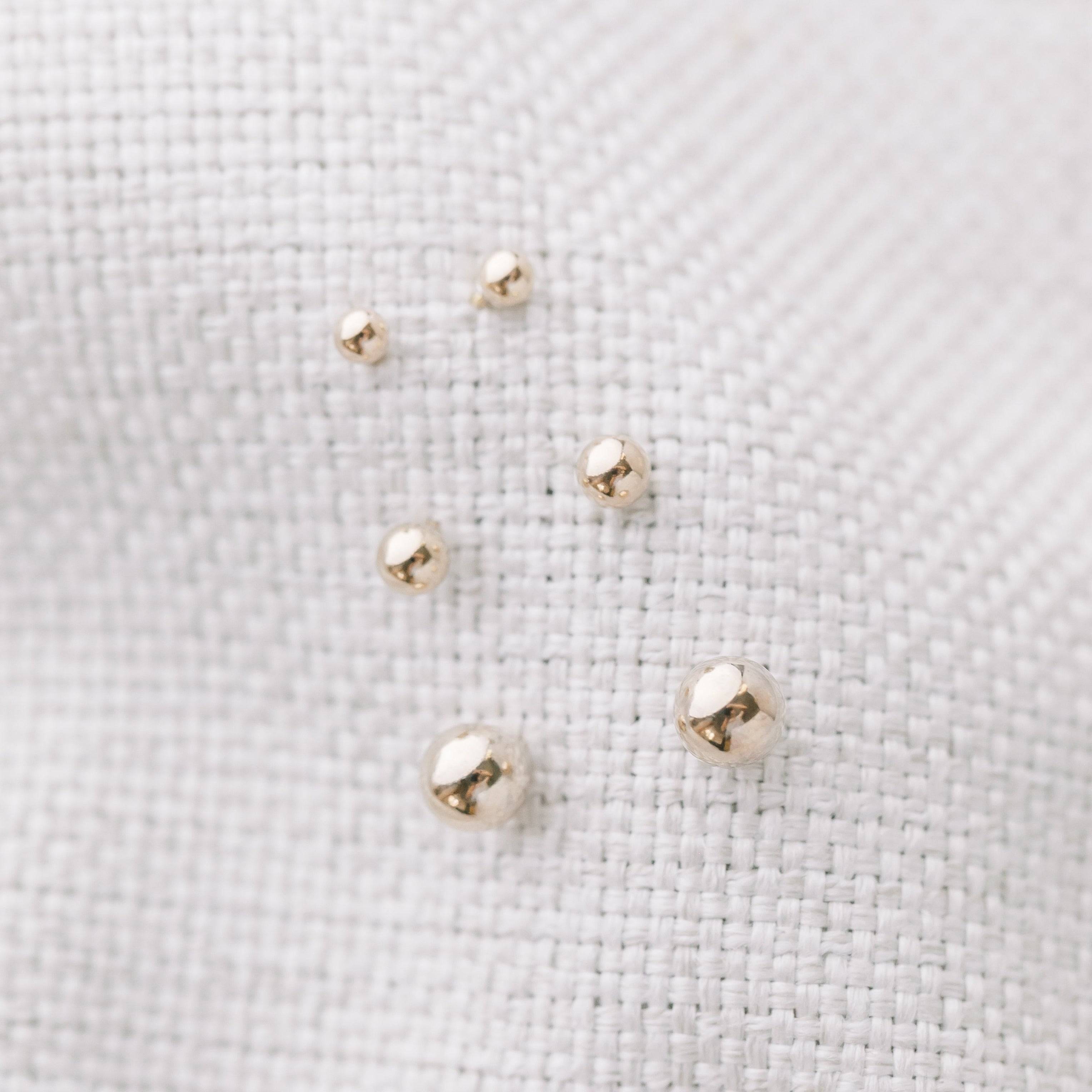 Assorted sizes of Ball Stud Earrings for Lobe & Cartilage in 14k Gold Fill displayed on white textured fabric. Waterproof and tarnish resistant.