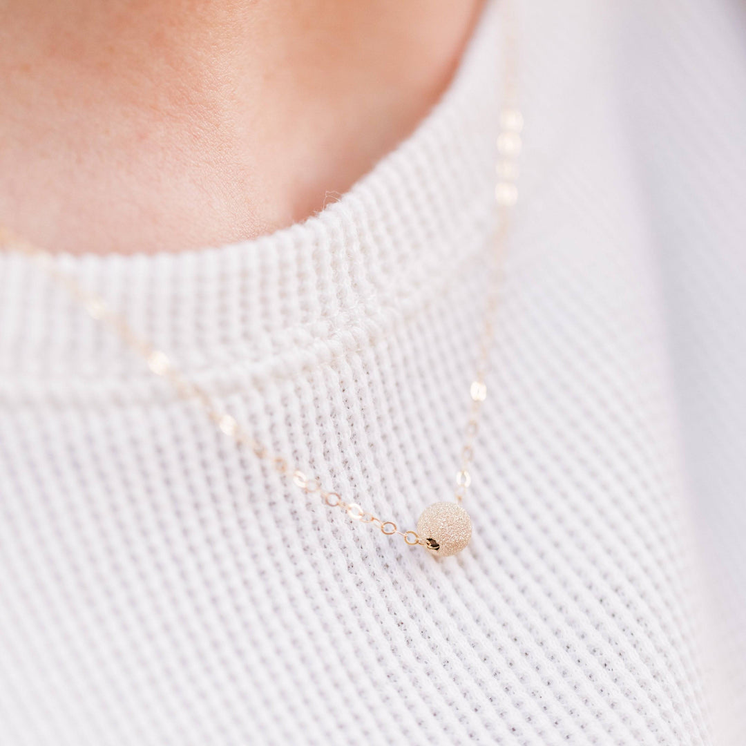 Layering Stardust Bead Necklace in 14k Gold Fill worn over a white textured top, showcasing its minimalist and elegant sparkle.