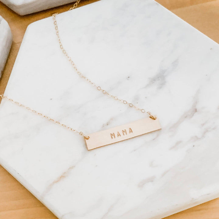 Hand Stamped MAMA Bar Necklace by Barberry & Lace Jewelry, 14k Gold Fill, displayed on a marble background, ideal for Mother's Day gifts.